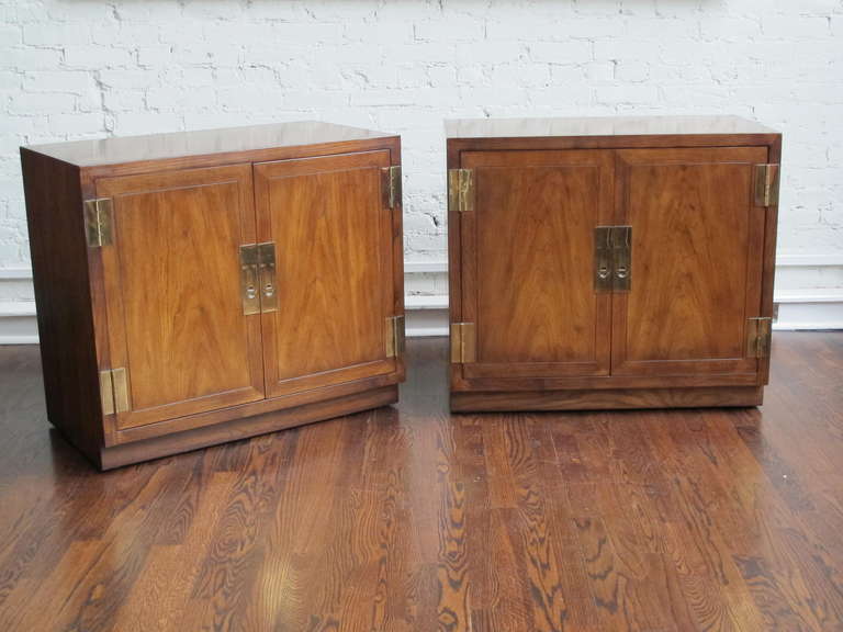 Pair of oak cabinets in a medium-brown, mottled finish with large brass recessed pulls and large surface-mounted brass hinges. Great bedside tables with ample storage.