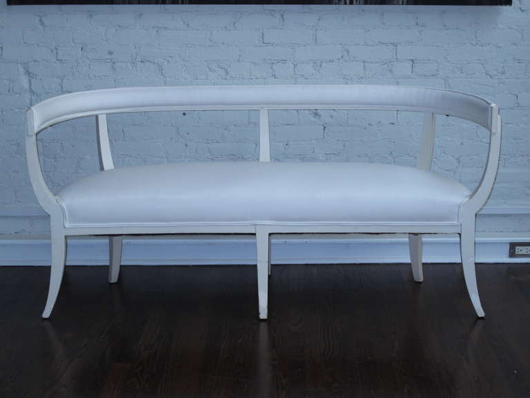 White painted pine Swedish settee with sweeping saber legs and barrel back. Tight backrest and seat currently upholstered in white cotton. Chips in white paint reveal earlier orange paint.