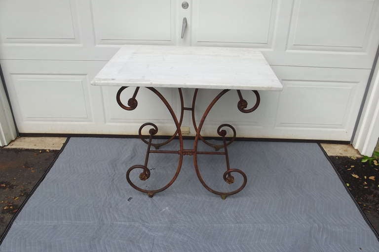 A classic French wrought iron butcher's table with a white marble top.  The table has an as found oxidized surface with remnants of the original paint and primer showing.  The original rosettes and knuckle retain part of their original gilding.  