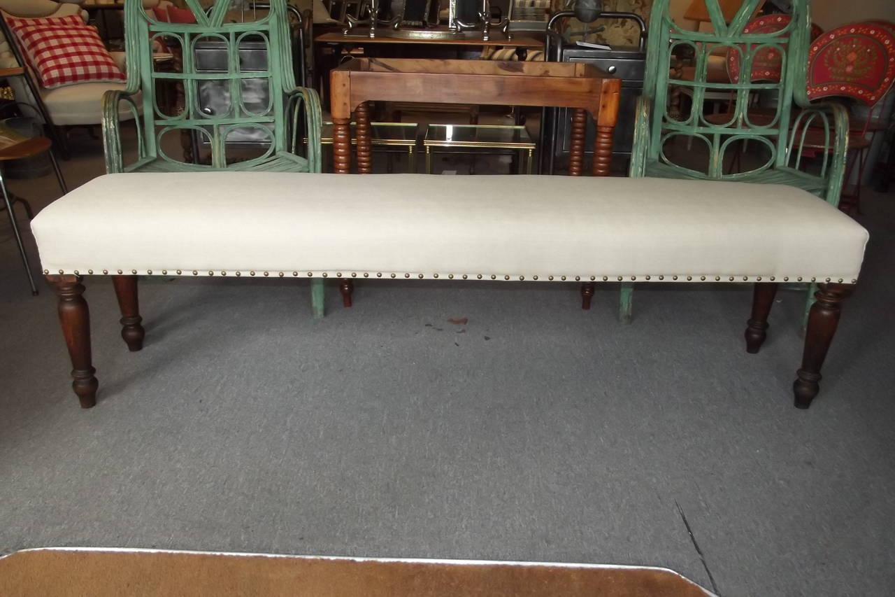 A late 19th century bistro bench with turned cherry legs and newly refinished in natural linen fabric with a French natural tack finish.  The perfect size for the foot of a king sized bed.  There are two of these benches available.