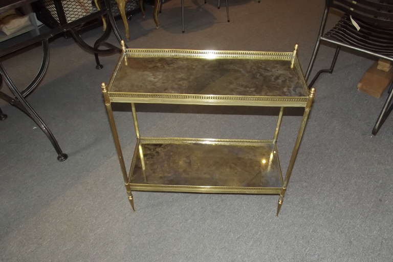 A two-tier French brass framed side table with distressed mirror tops attributed to Maison Jansen. The table is in excellent overall condition. The brass frame has no damage and pleasing, very slight tarnish to its surface. The glass is in perfect