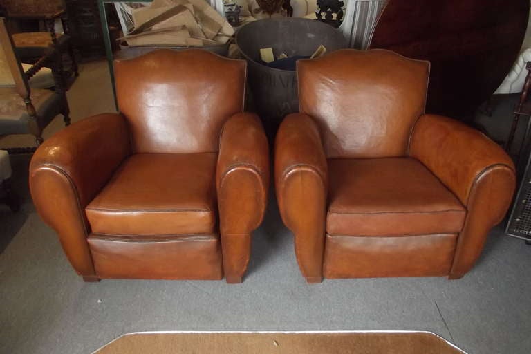 A large-scale pair of French mustache-back leather club chairs. These chairs have completely original leather which has been professionally restored in France. Also the suspensions of the chairs have been completely restored and the chairs sit very