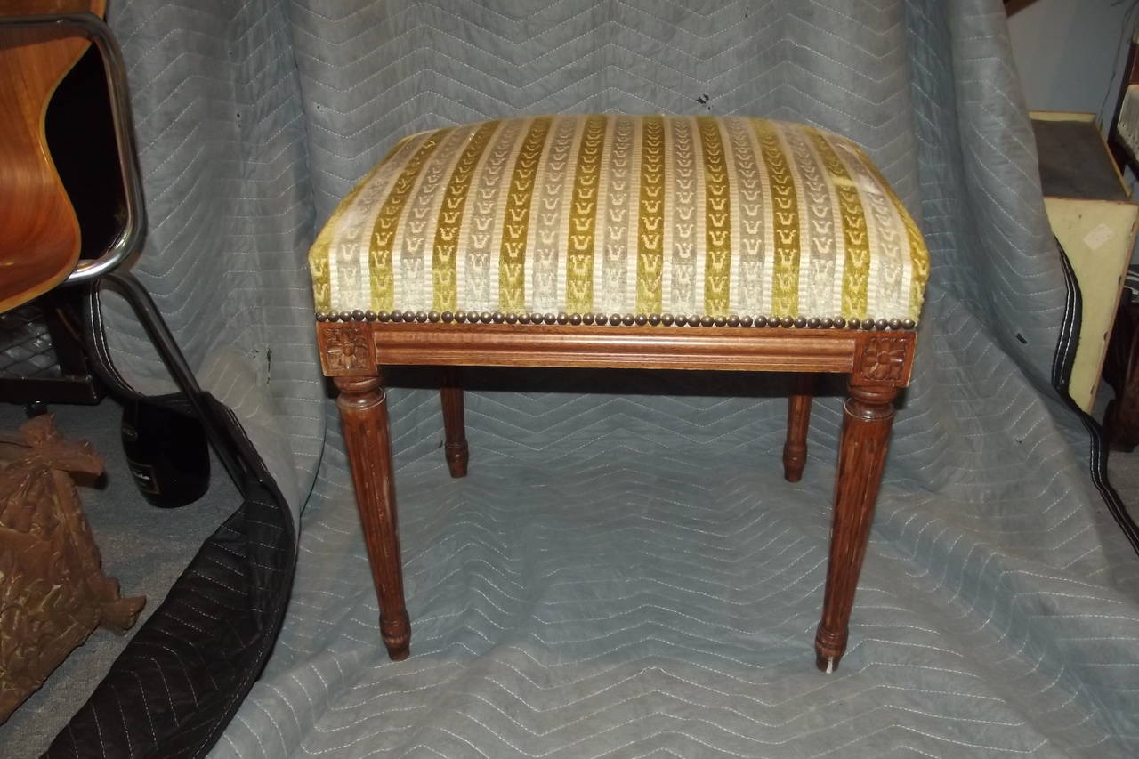 A small bench or ottoman in the style of Louis XVI in its original mellow brown finish. Upholstery is not new but is recent and in usable condition without stains or tears.
