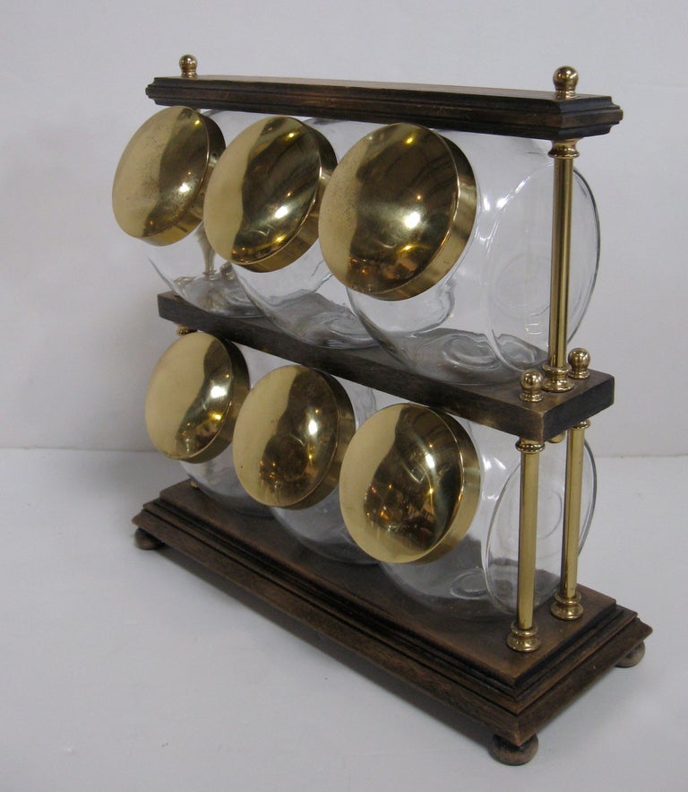 Unusual canister set comprised of six glass canisters with brass lids.  These are displayed in a two tier wood stand with brass rods and finials.
To extract canisters, brass rods are loosened and wood shelf is lifted.