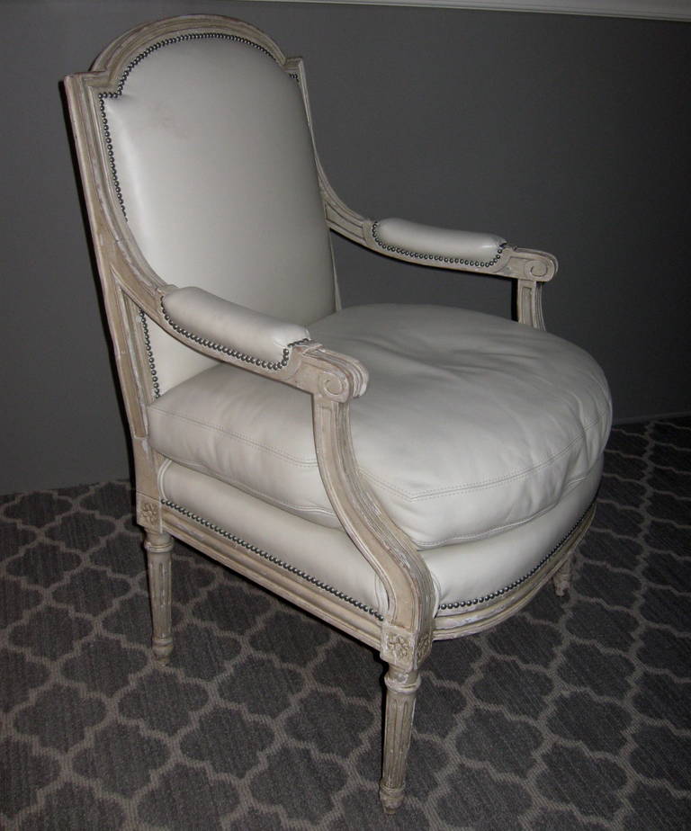 Pair of Louis XVI style armchairs. These French fauteuils chairs have been recently reupholstered in a Holly Hunt cream leather, with silver nailheads. Removable cushions are feather and down. Frames are painted wood.