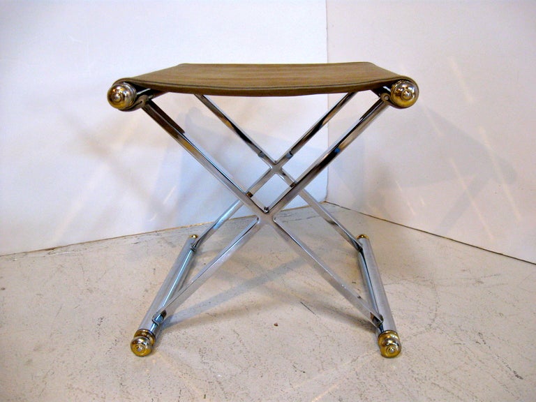 Pair of polished chrome and brass stools / benches, in the neo-classical style.  With ultrasuede  seats, these small but sturdy stools feature an X form base with brass finials at each end.
There is a very minor spot that has faded in color on one