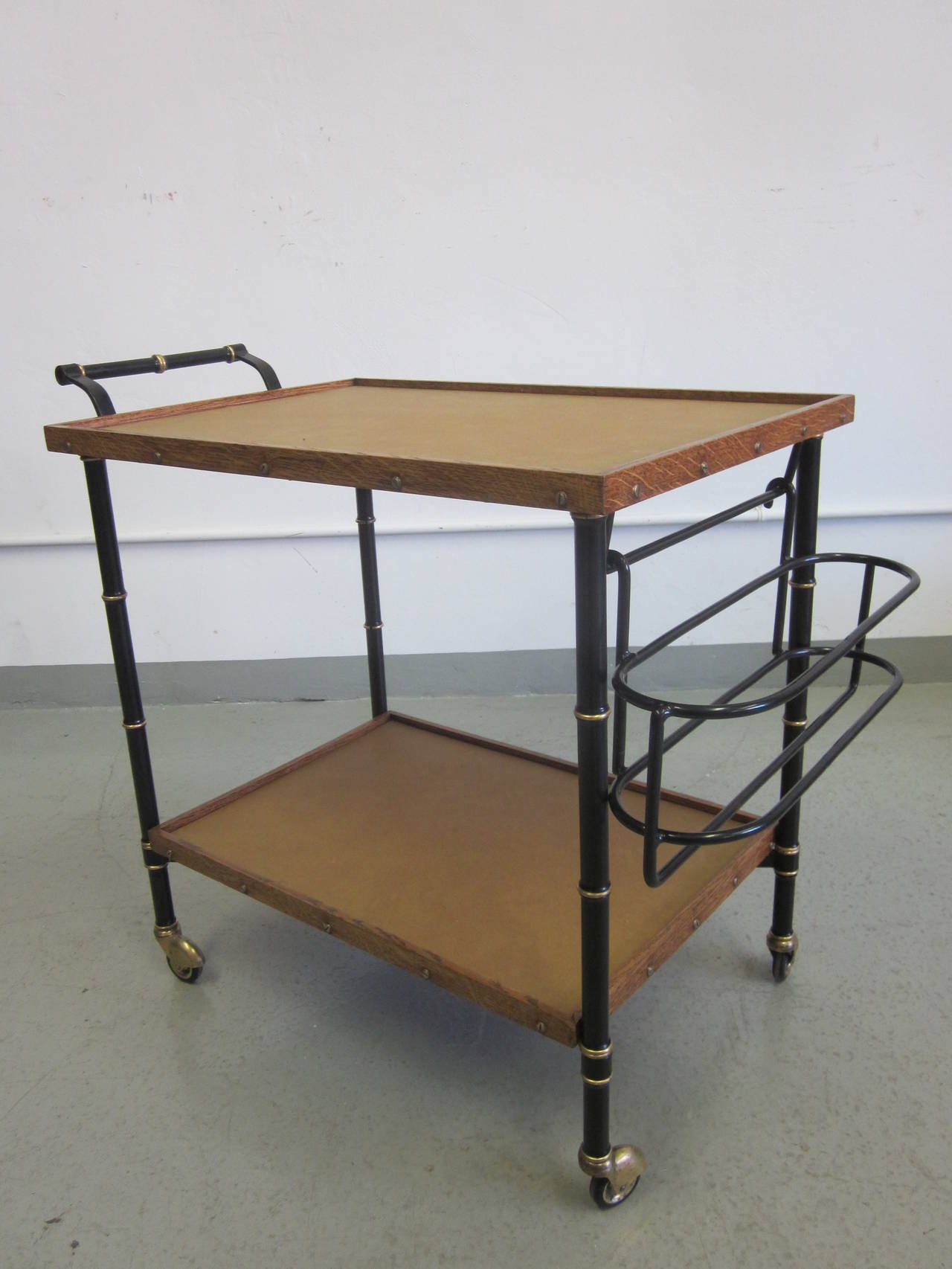 Important French Mid-Century bar cart by French master designer, Jacques Adnet (France, 1901-1984) showing influences of modern and neoclassical design. 

The cart is double level with a detachable enameled steel bottle rack and composed of
