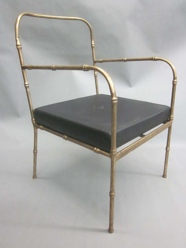 A Rare and elegant pair of French Mid-Century Modern style lounge chairs, armchairs, club or slipper chairs in the manner of Jacques Adnet. The chairs are composed of a delicate gilt iron faux bamboo frame and legs and with the seats in black faux