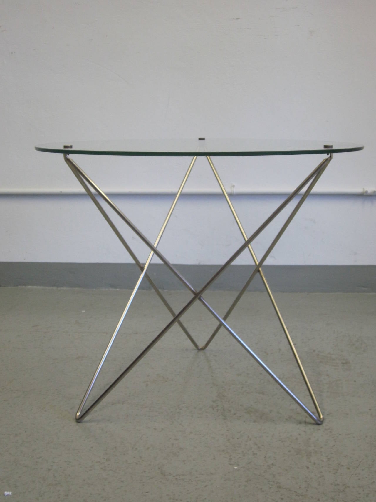 Elegant pair of Italian Mid-Century Modern end tables in stainless steel supporting round pierced glass tops.

The structures are composed of sober tripod frames that intersect at angles forming a neoclassical X-form. The glass is pierced and held