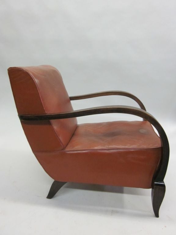 Pair of French Mid-Century leather club chairs or lounge chairs set in a bold wood frame with sweeping curved arms and rear saber legs. French Art Deco classics that have Modern sensibility.
