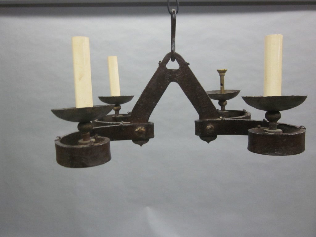 French early 20th century arts and crafts hand-wrought iron chandelier with four arms. The piece is well designed with two double arcing stems and features hand-hammered and partially gilt ironwork. Its small size is excellent for smaller spaces but