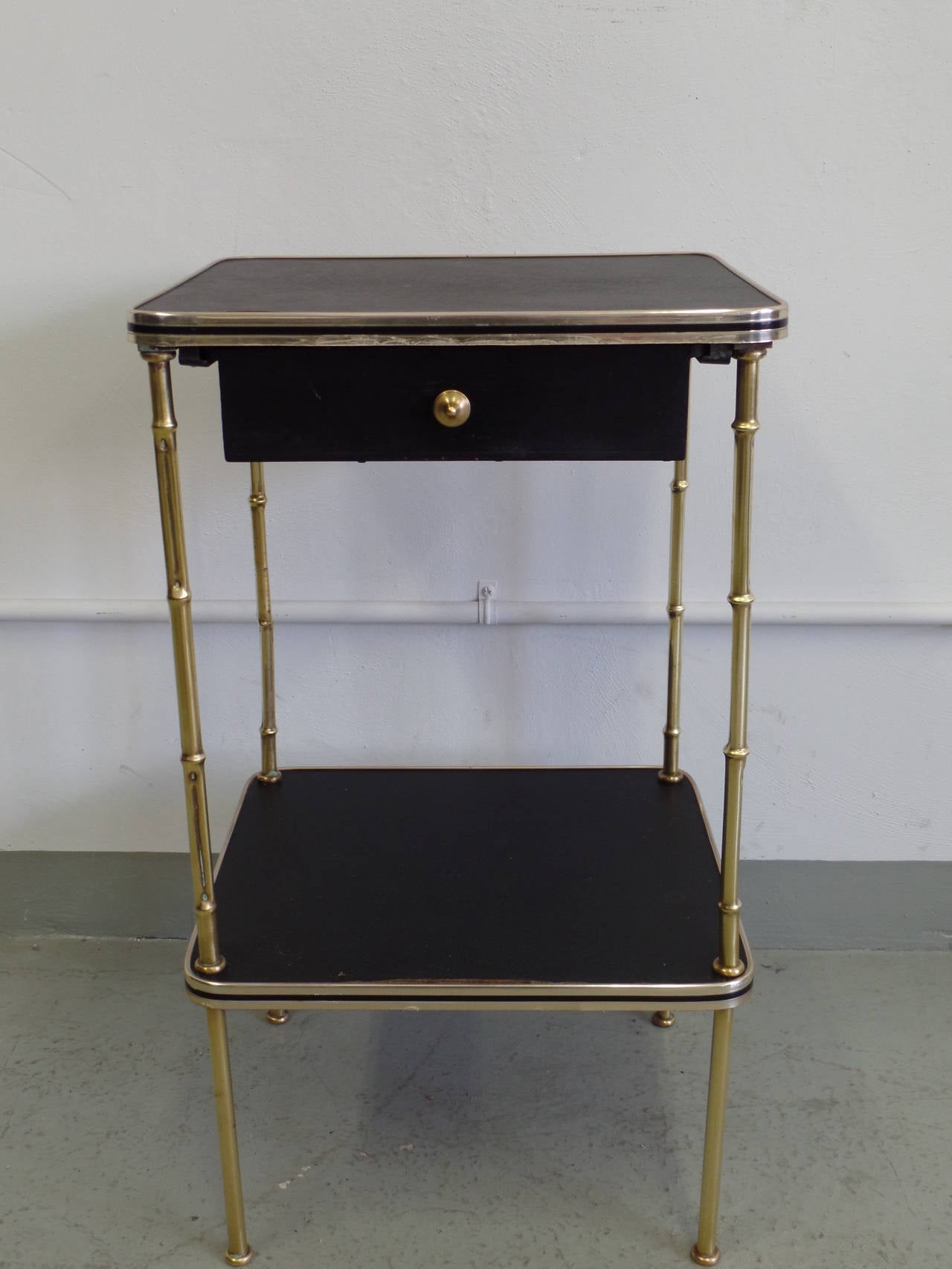 Rare and important pair of French, Mid-Century end tables or nightstands in the Modern Neoclassical spirit with solid brass faux bamboo legs and details and faux leather tops by Jacques Adnet. Each table is double level and has one drawer with brass