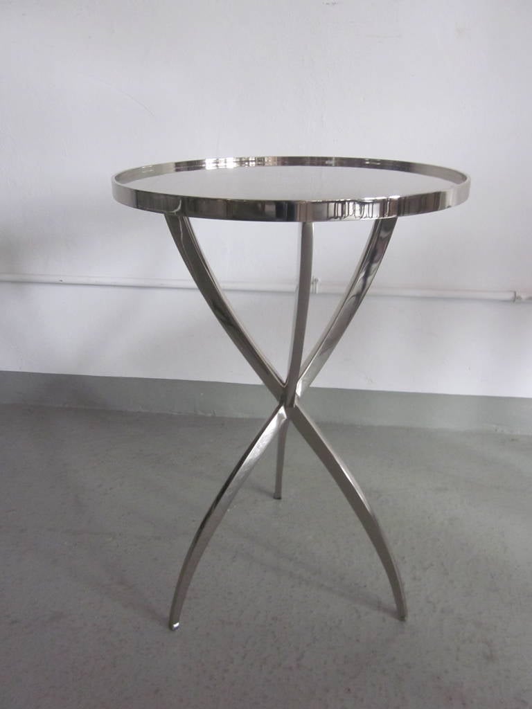 Elegant and timeless pair of French Mid-Century style, polished nickel gueridons or end tables or nightstands in the modern neoclassical tradition with delicate tapered tripod legs. The pieces are conceived with the highest quality of materials and