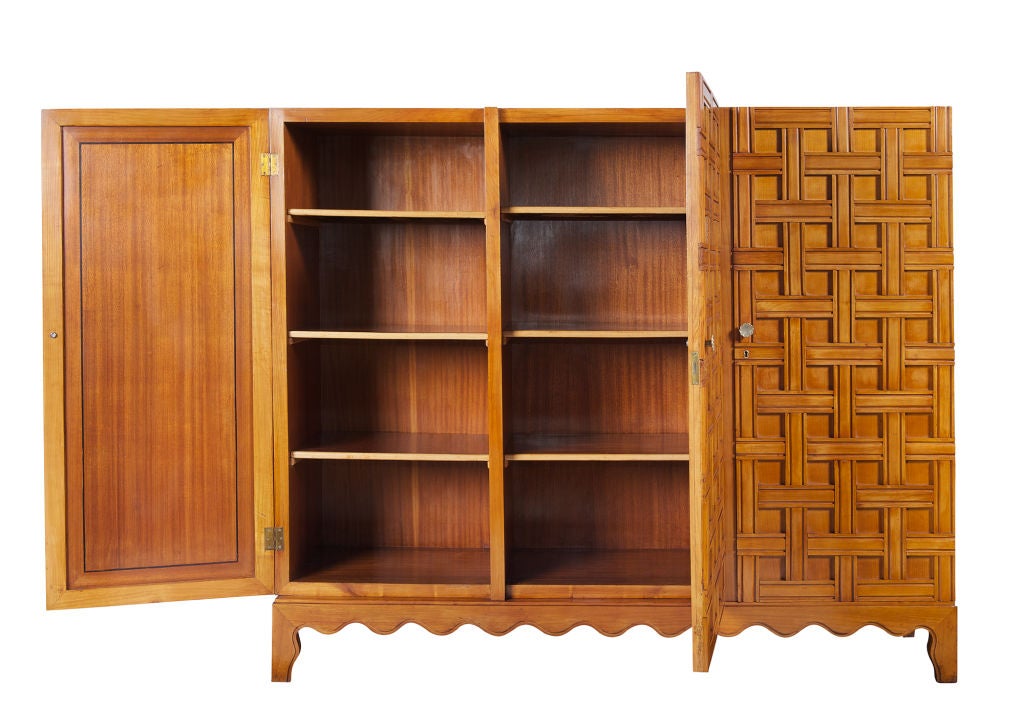 A cherry wood cabinet with three doors carved in the motif of an open basket weave. The interior side doors inlaid in ebony, two doors revealing six mahogany shelves and one concealing an illuminated bar with four mirrored drawers with lucite pulls