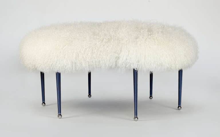 This large round ottoman has a white mongolian wool cushion and navy blue leather wrapped legs.  The legs are accentuated with white stitching and chrome feet.  This item is located in our space in the 1STDIBS@NYDC showroom, 200 Lex
