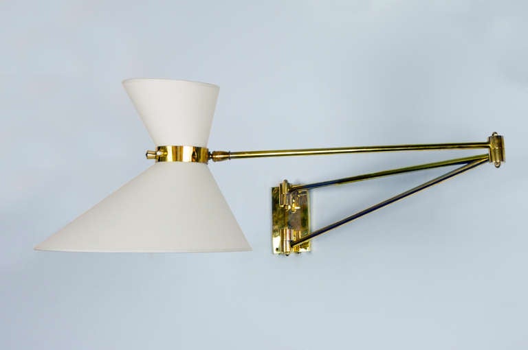 This single sconce with its polished brass wall support has diabolo asymmetrical linen shades. The fixture has clean angular lines and the double socket to light up each shade, Sockets can be turned on separately.   Larger shade has a 14