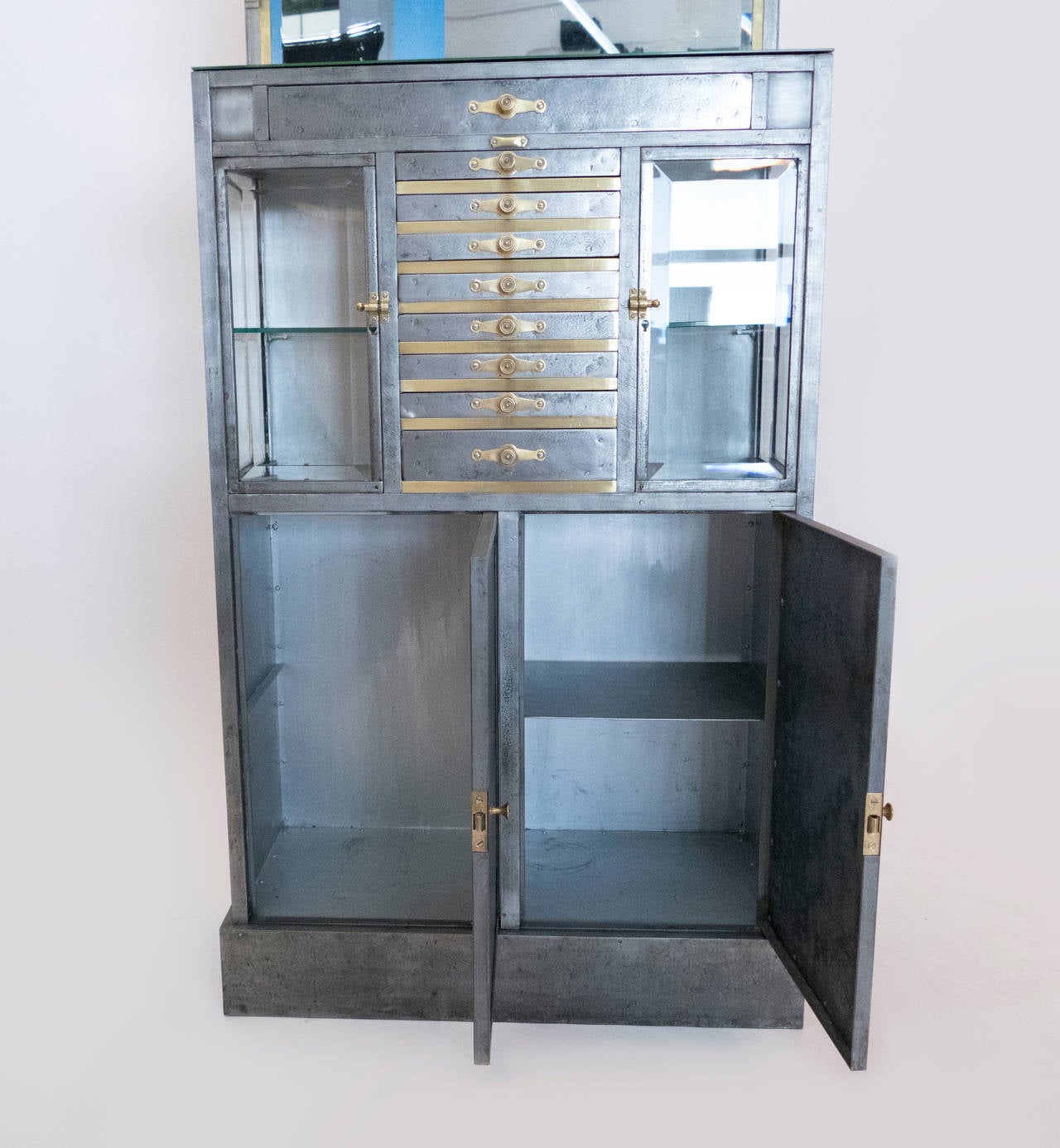 This polished steel cabinet from a turn of the century dentist office has beautiful brass elements and beveled glass.  Perfect condition,  polished and lacquered to provide for a long durable finish.  The original beveled mirror tops the piece.
