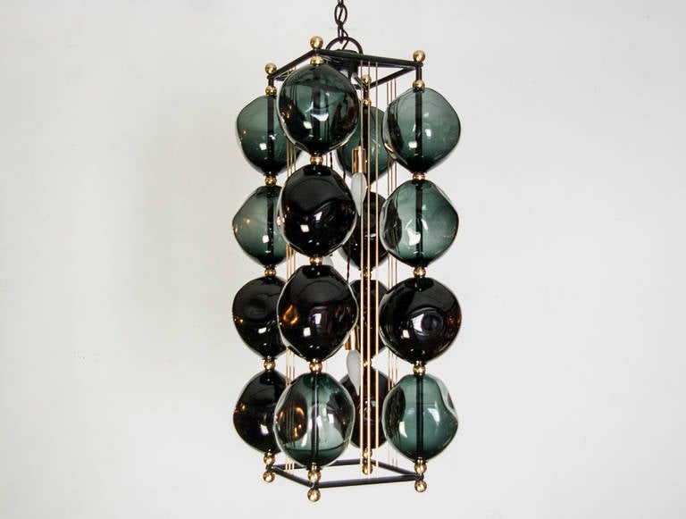 16 orbs handblown in black glass are assembled on a steel frame with a gun metal patina. The chandelier has brass accents. The light uses three candelabra based sockets, Max wattage 60 each bulb. The fixture is located in our space in the