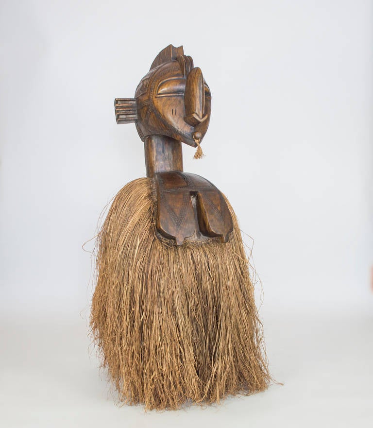 An impressive work of art.  This shoulder mask from carved wood was used in the tribal celebrations.  Worn over the shoulders, the raffia has been replaced. It has been placed on a  movable base.