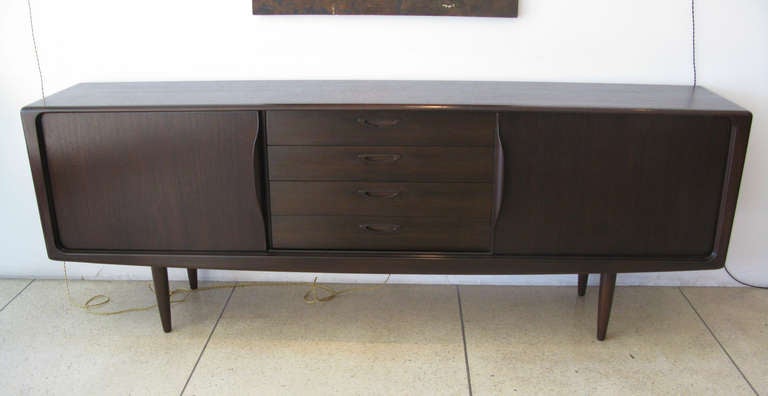 Teak sideboard/credenza designed by H.W. Klein for Bramin, Denmark.  Has 4 center drawers and 2 side doors that slide open to reveal a single shelf behind each.  Finished in a dark chocolate brown.