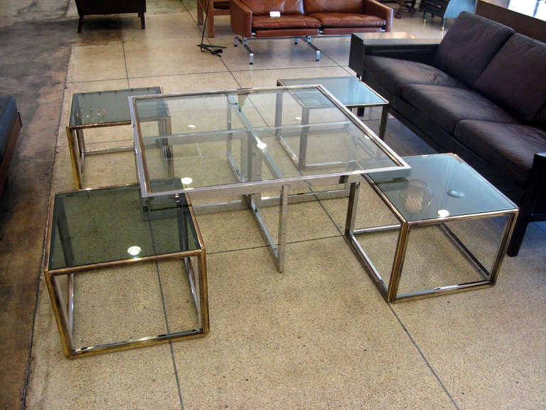 Maison Maison Charles.  Le cadre carré a une finition originale en laiton et métal chromé avec un bel âge.  Des plaques de verre fumées sont insérées de manière lâche pour créer les surfaces de la table. Les quatre tables latérales ajustées mesurent