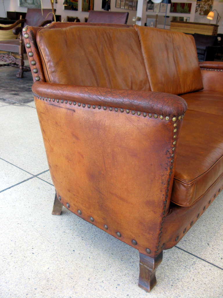Aged leather 2 person sofa.  Cognac leather has a beautiful patina from age.  Brass nail head detailing & stained wood feet.