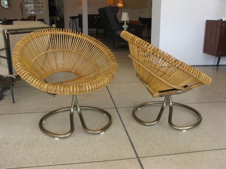 Pair of unique swivel chairs with woven rattan seats and antiqued brass plated steel bases.  Chairs swivel 360 degrees.  Seat measures 15.75