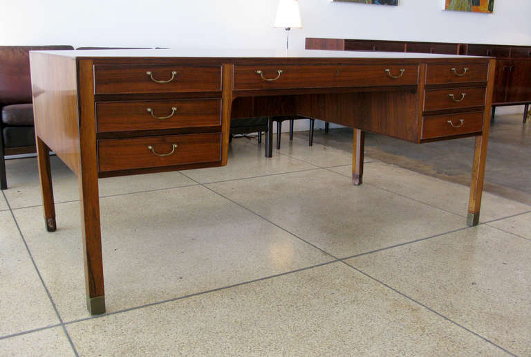 Rosewood desk designed by Ole Wanscher with 7 front drawers with brass drawer pulls.  Aged brass capped feet.  The desk surface is slightly bowed from age, however this does not impact the structural integrity.  Please note the desk was photographed