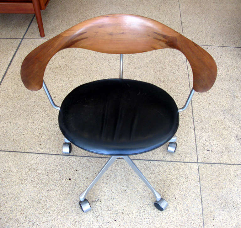 Rare late model swivel desk chair designed by Hans J. Wegner and produced by Johannes Hansen Cabinetmakers.  Original aged black leather seat and teak back rest.  Rare die-cast steel base with five legs on castors.  Seat height: 17