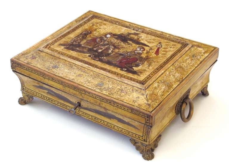 An elegant English Regency yellow-lacquered chinoiserie jewelry box; the splayed top centring a tranquil landscape scene resting on a conforming body raised on gilt metal feet and flanked by bold ring handles.