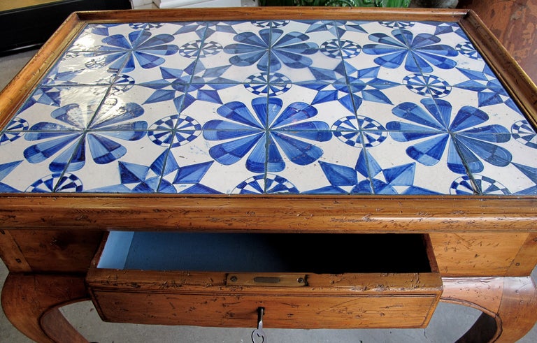 A shapely Danish rococo style stripped pine single-drawer side table with delft blue-and-white tile top; the inset 18th Century delft tile top of pinwheel and geometric design; above a scalloped apron fitted with a single drawer all raised on