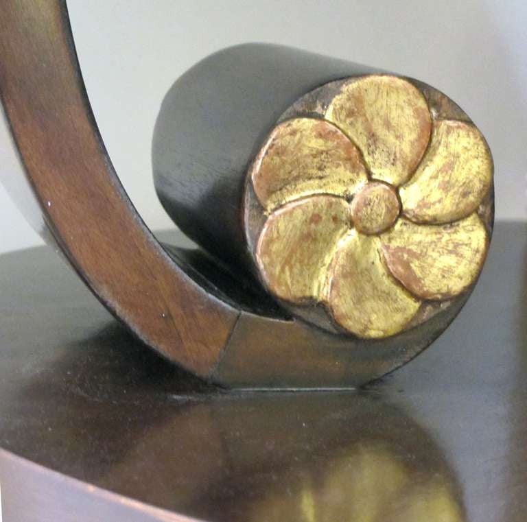 A handsome American art deco style mahogany cocktail/center table with scrolled legs; the well-figured shaped top raised on 3 dramatically scrolling supports adorned with gilt foliate elements all over a lower shelf
