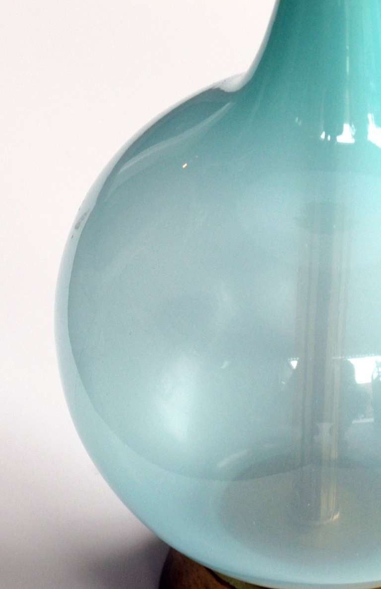 A shapely pair of Italian mid-century translucent aqua art glass bottle-form lamps; each softly-colored lamp with long neck above a bulbous body; raised on giltwood base