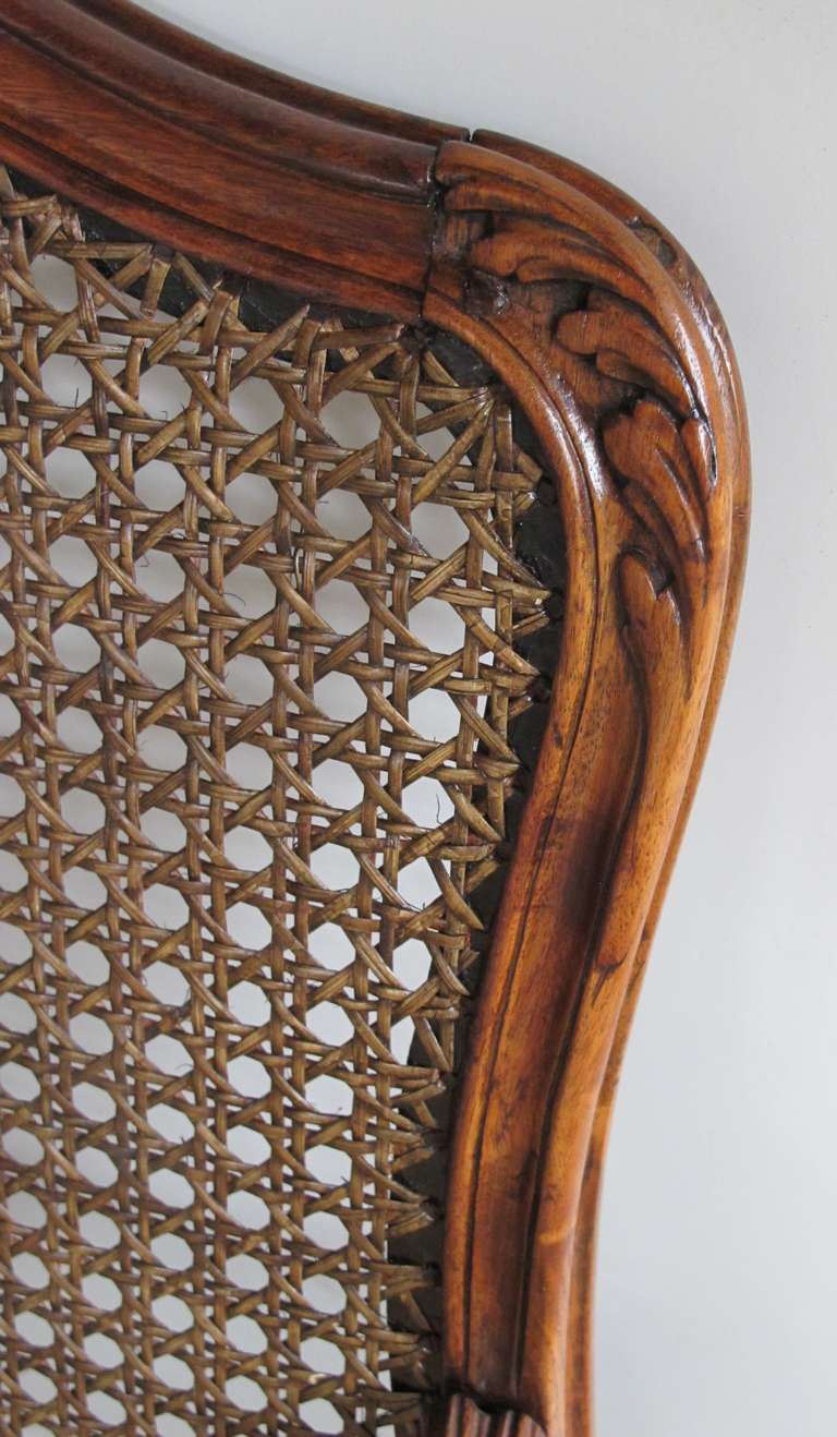 An elegant pair of French rococo beechwood open arm chairs with caned seat and back; each with a cartouche-shaped caned back above a caned seat flanked by scrolling arms; raised on graceful cabriole supports