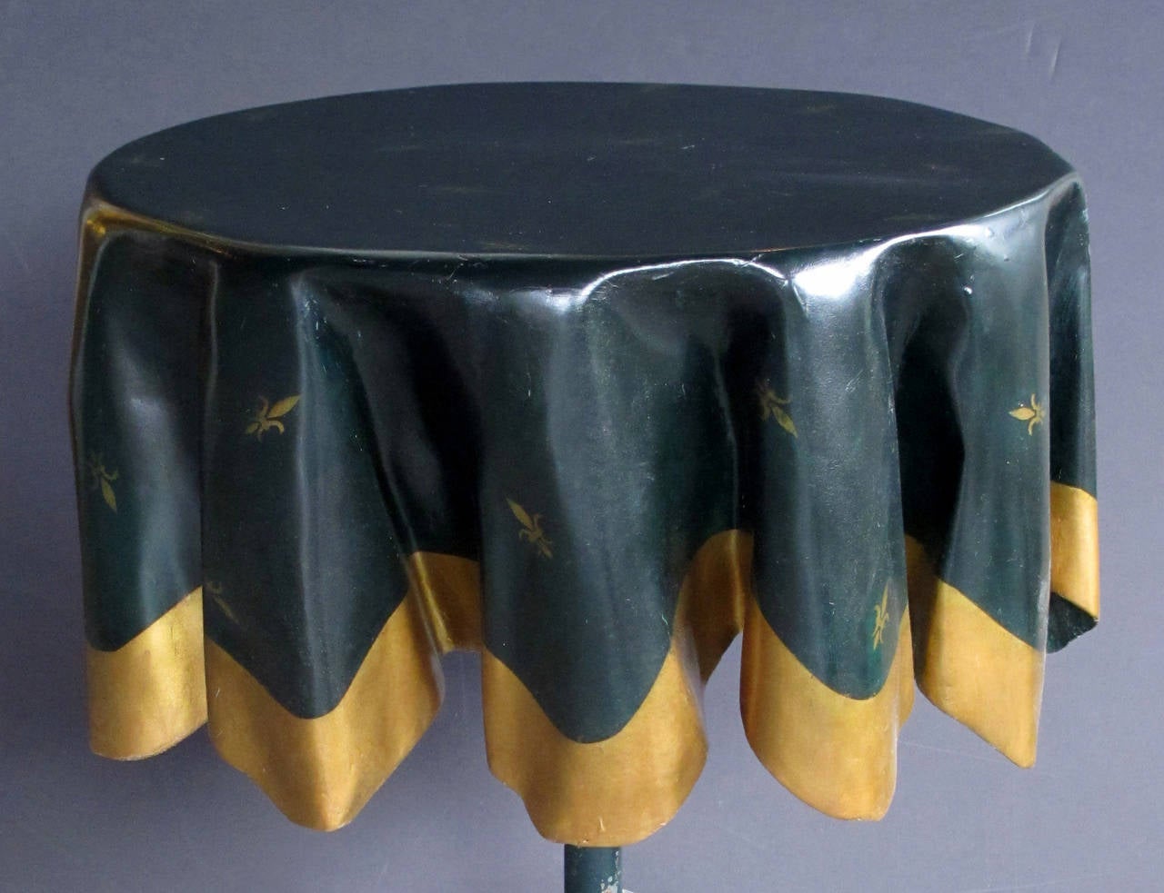 A whimsical French 1960s fiberglass 'drapery' table with iron tripod base; the winter green fiberglass top depicting a draped tablecloth adorned with gilt fleur-de-lis decoration; raised on an iron tripod stand.