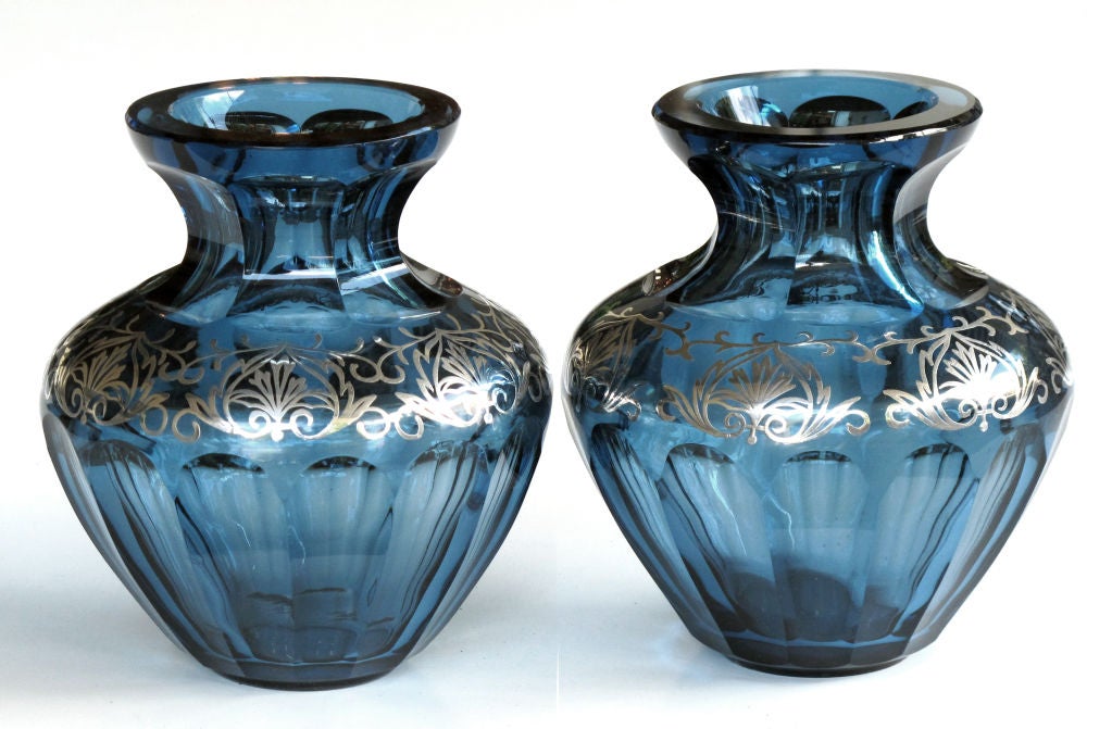 A good quality and thickly-modeled pair of Bohemian art deco sea-blue crystal vases with silver overlay; possibly by Moser Glassworks; each with faceted everted neck above an ovoid body with a reticulated collar of silver overlay above a faceted body