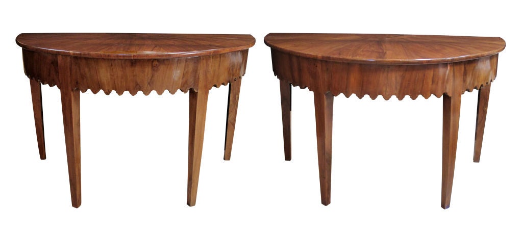 A handsome pair of Italian neoclassical olivewood-veneered demilune console tables with scalloped apron; each with half-round top of well-figured pie-shaped veneer above a scalloped apron; raised on tapering quadrangular supports