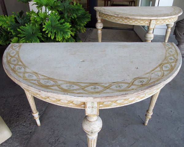 A charming pair of Danish neoclassical ivory painted demi-lunes with ochre highlights; each half-round top with interlacing fret band above an apron with similar decoration; supported on tapering legs with bulbous cap over a faux fluted support; can