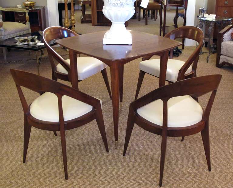 A stylish French modernist 1950's mahogany game table with four matching chairs; the square shaped top of striped tiger mahogany raised on turned supports with brass toupie feet; each barrel back chair sloping to the seat raised on elegant tapering
