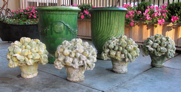 A delightful set of four French cast stone compotes; each with everted ribbed basket overflowing with plump fruit and bold flower heads surrounding a perched bird