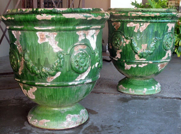A boldly-scaled pair of French emerald-green glazed terra-cotta Anduze garden urns; each large-scaled urn with everted lip above a bell-shaped body adorned with raised stylized floral bosses surrounded by curvaceous garland swags; raised on