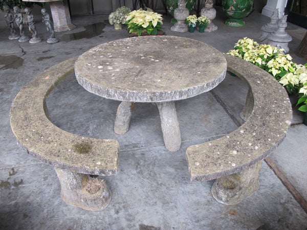 A rare and whimsical French faux bois concrete circular table with 2 arched benches; the thick circular top raised on a tripod base of robust faux bois tree trunks; surrounded by 2 large curved benches raised on tree trunk supports