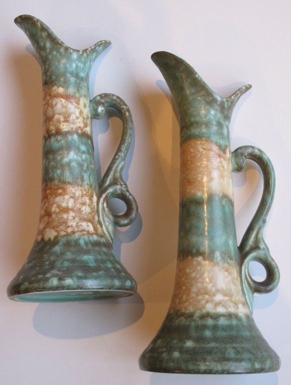 A rare pair of German Arts & Crafts matte glazed pottery pitchers; incised 'Colmin' stamped 'Germany'; each of graceful form with pinched mouth above a flared body with scrolled handle; alternating celadon and ochre glazed bands.
