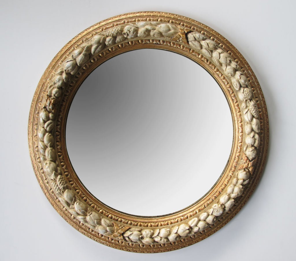 A well-carved English Georgian style ivory painted and parcel-gilt circular mirror; the original round plate within a carved wood stepped frame with egg and dart molding surrounding a ribbon-tied festoon garland.