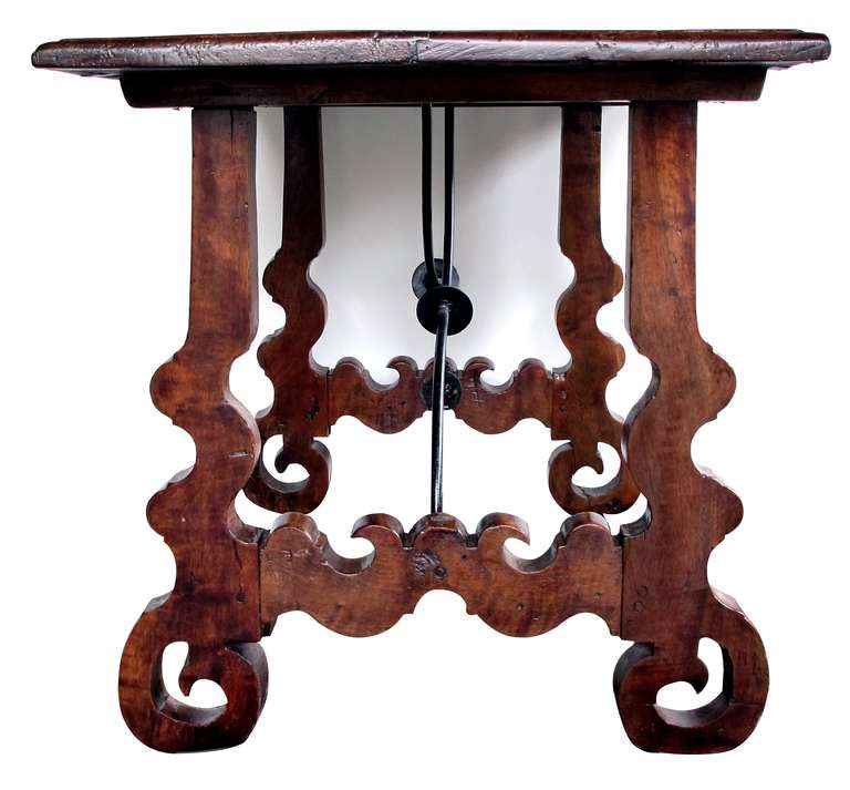 A rustic and well-patinated Spanish baroque style walnut trestle table with iron stretcher; the rectangular plank top supported by h-form trestle legs joined by a curvaceous iron x-stretcher; composed of 18th & later elements