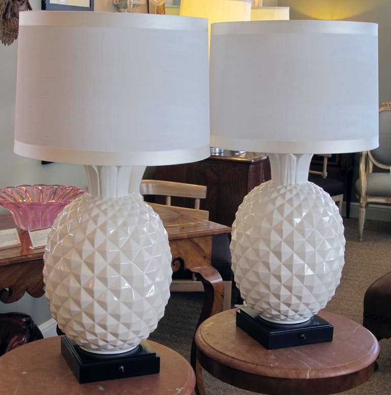 A robust and large-scaled pair of Italian 1960's white ceramic pineapple-form lamps; each portly lamp depicting a plump pineapple resting on an ebonized base