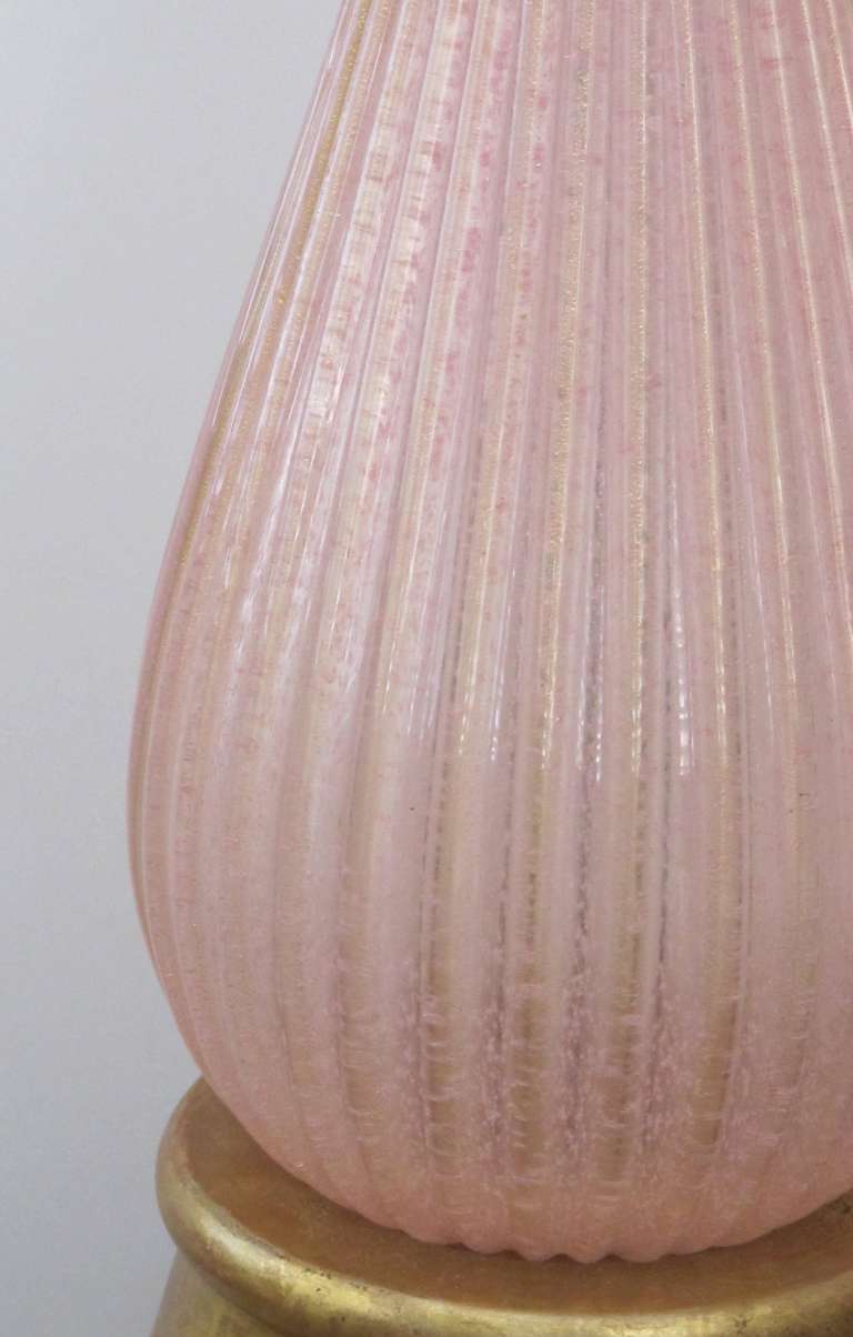 A subtle pair of Murano mid-century teardrop form pink ribbed gold aventurine lamps; each with long flaring neck above a bulbous body; raised on a giltwood base