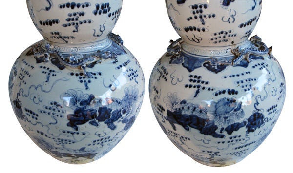 A striking and large-scaled pair of Chinese blue and white double-gourd porcelain vases; each with everted lip above a double-gourd body adorned overall with playful fu dogs amid stylized clouds; with applied dragons at the shoulders
