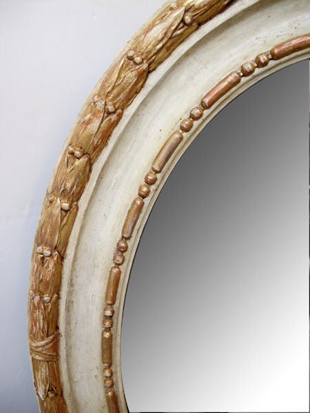A large-scaled English George III style ivory painted and parcel-gilt carved wooden oval mirror; the original oval plate within a boldly-carved wooden oval mirror; the original oval plate within a boldly-carved coved frame with beaded inner border