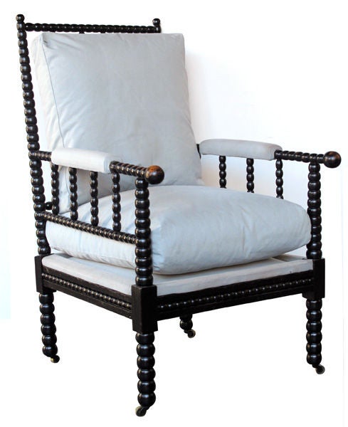 A handsome pair of English Victorian ebonized bobbin turned open armchairs; each with tall openwork back and sides of bobbin turned ebonized wood; raised on similar turned legs ending in casters; with down filled loose cushions